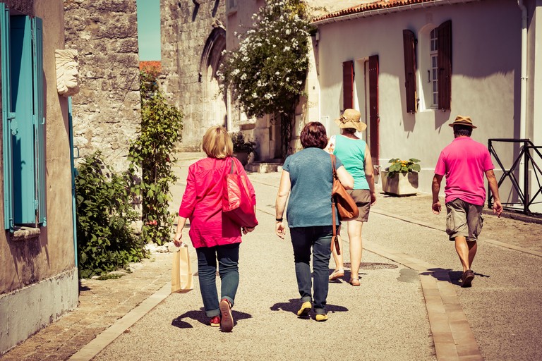 Back View Of A Group Of Tourists Walking In A Village In Summer
